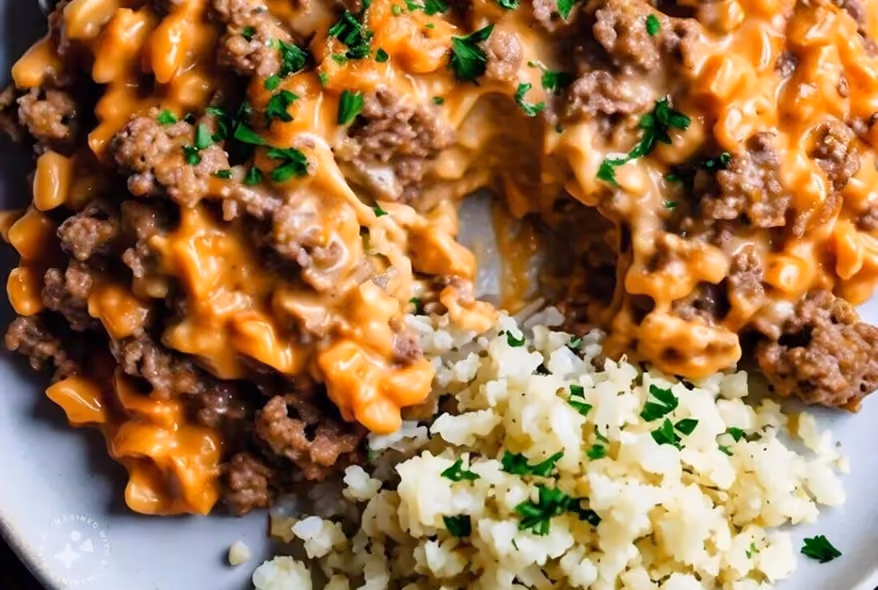 Plate with ground beef covered in melted cheese sauce and a side of cauliflower rice garnished with chopped parsley.