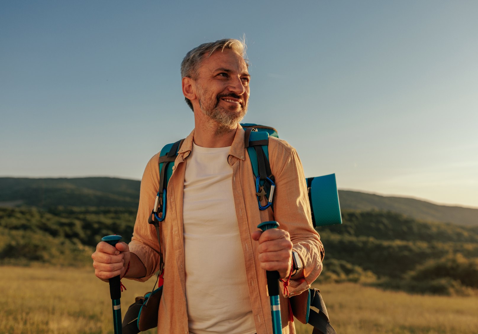 Smiling hiker with trekking poles at golden hour