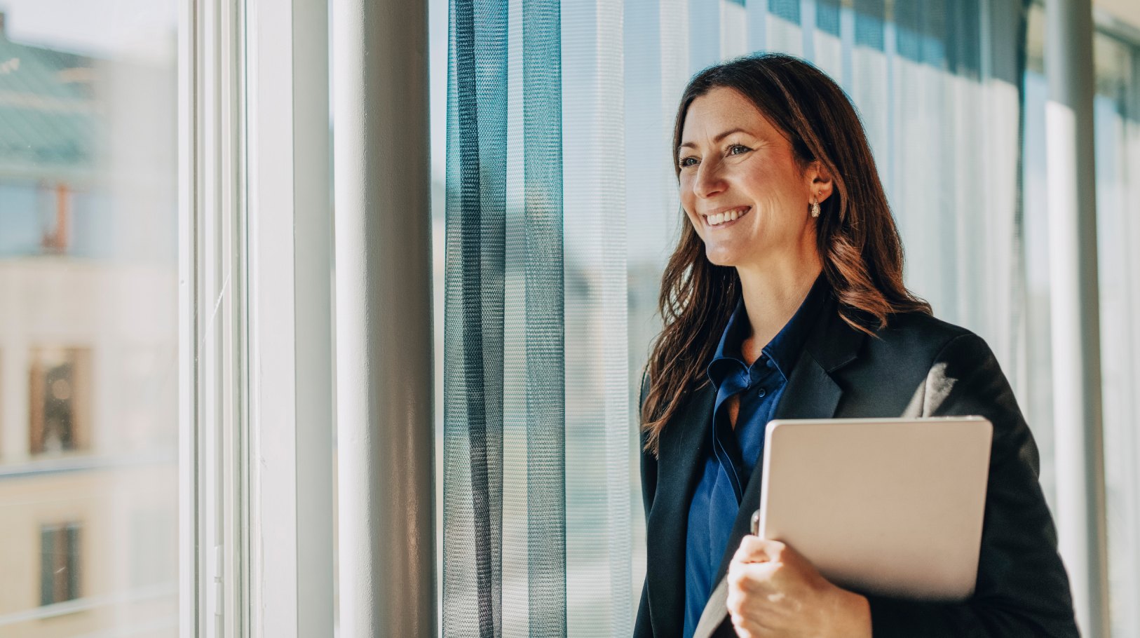 Benefits consultant smiling, holding a laptop by an office window