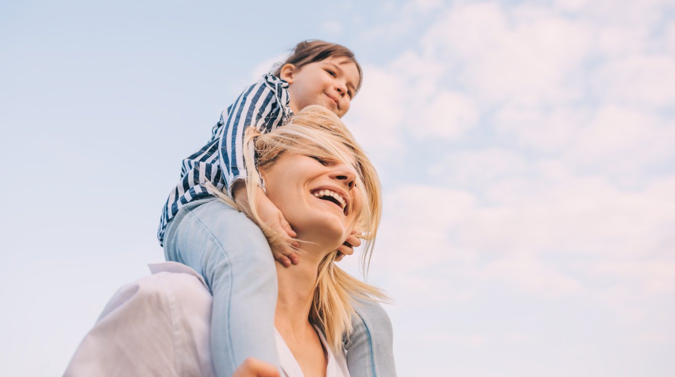 Smiling mother carrying her young daughter on her shoulders outdoors