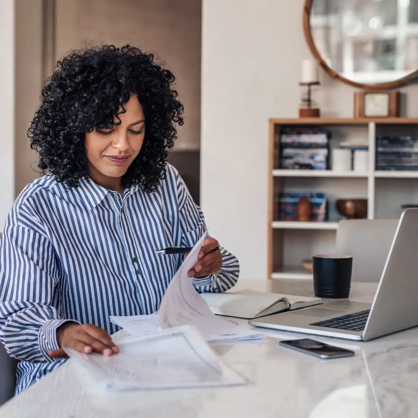 A woman with long blonde hair, smiling and holding a laptop, wearing a light-colored vest over a shirt.