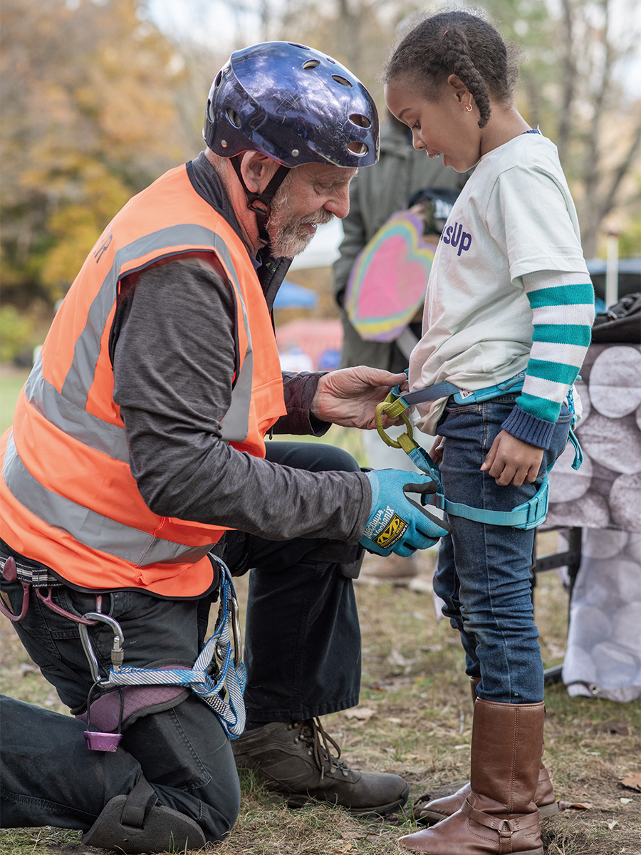 Man showing girl how to secure safety harness for tree climbing.