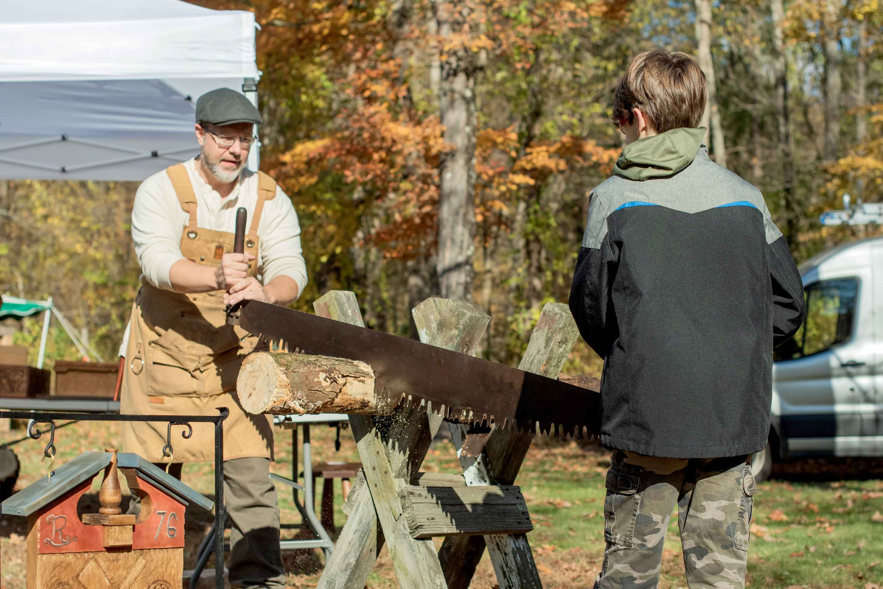 Man and boy using two person saw to saw a tree trunk.