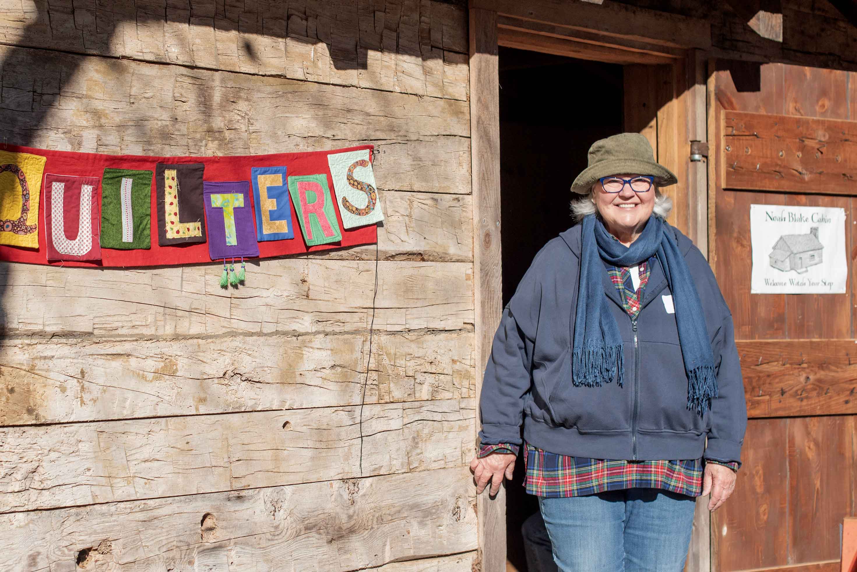 Friendly woman smiling at camera next to sign that says "Quilters."