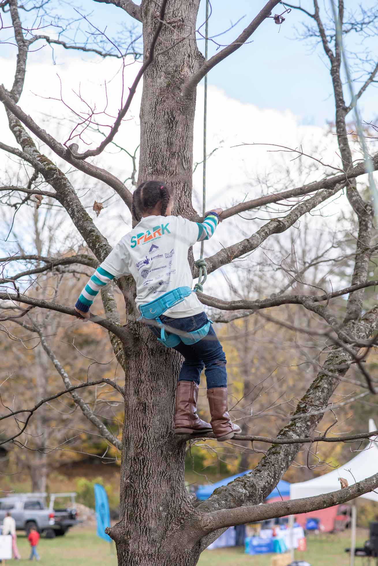 Girl climbing tree while wearing safety harness.