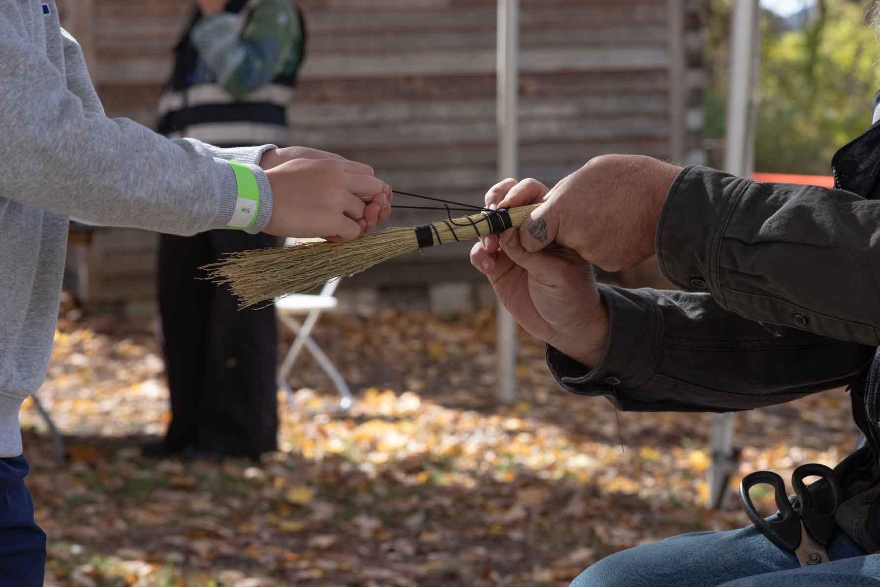 Boy tightly drawing twine around bristles to make broom.