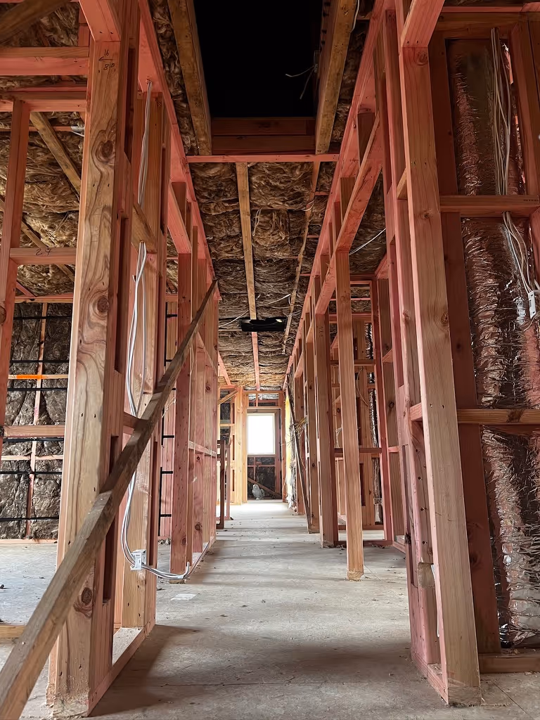Interior of a house under construction showing wooden framing and insulation with a window at the end of the hallway.