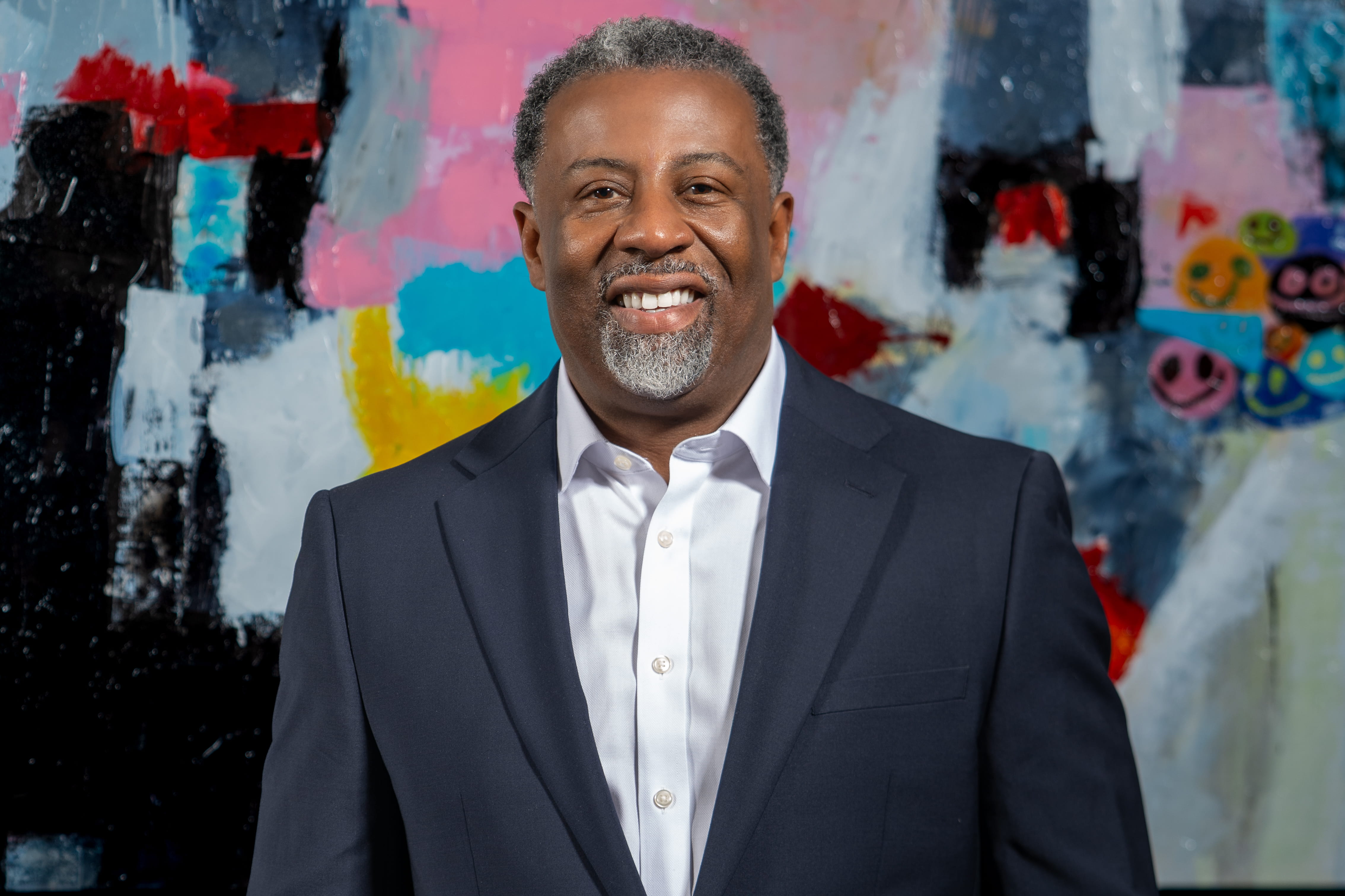 John Bettis wearing a navy blazer and white shirt against colorful abstract background.
