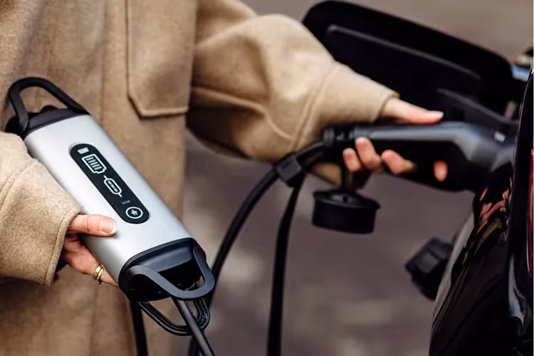 Eine Frau hat Ladekabel in der Hand und steckt Fahrzeug an