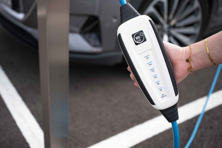 Hände halten das blaue-weiße Ladekabel, welches das Fahrzeug aktuell lädt, APDT12501001