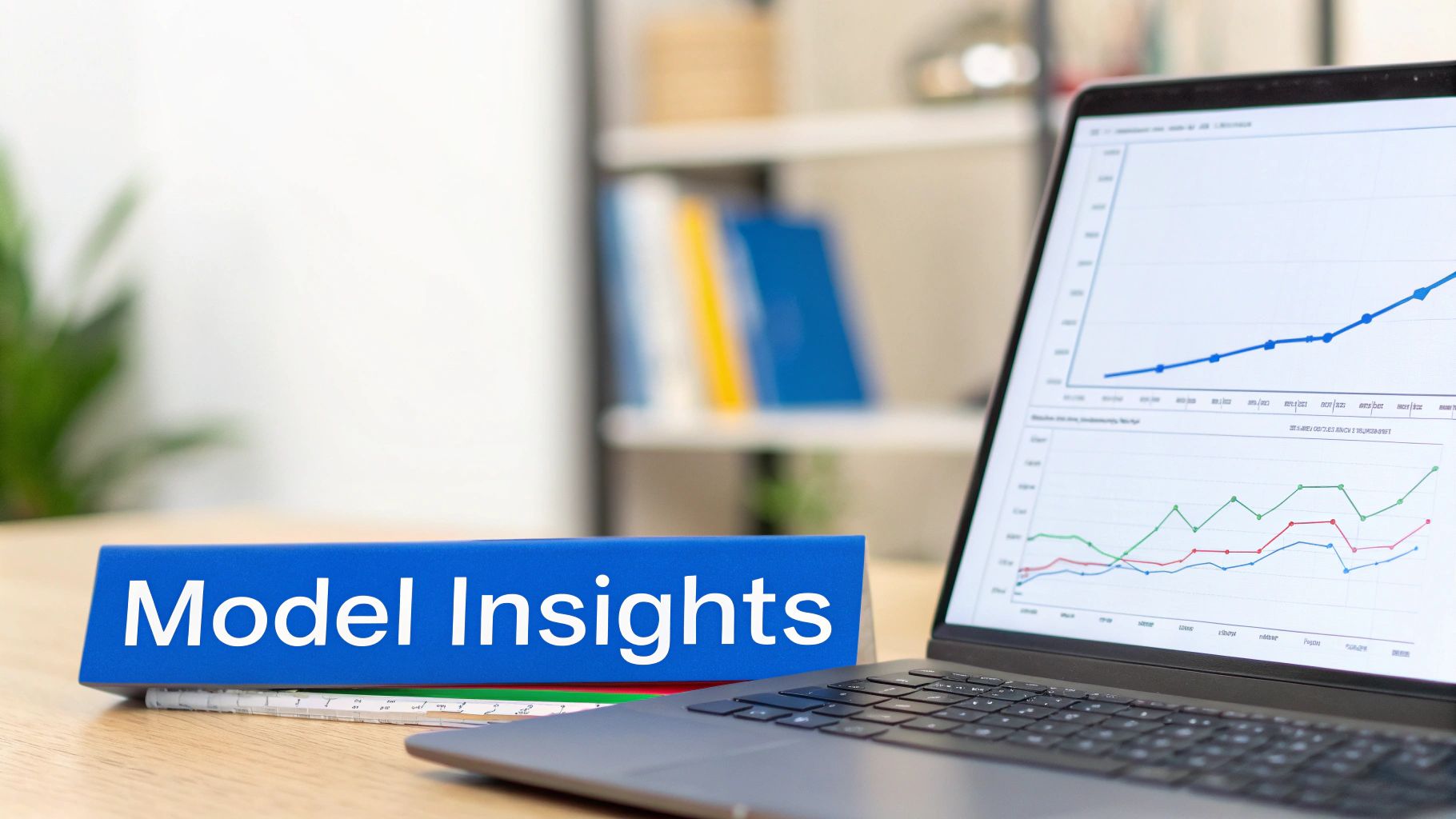 A blue 'Model Insights' binder on a wooden desk next to a laptop displaying data graphs.