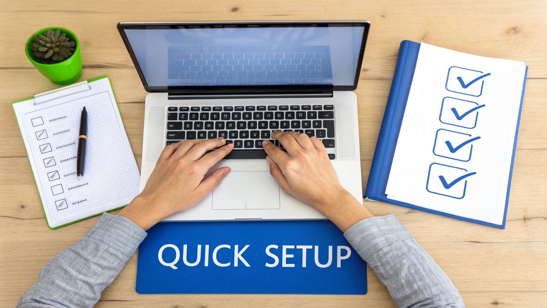 Overhead shot of person typing on a laptop, with checklists, pen, and plant on a wooden desk.