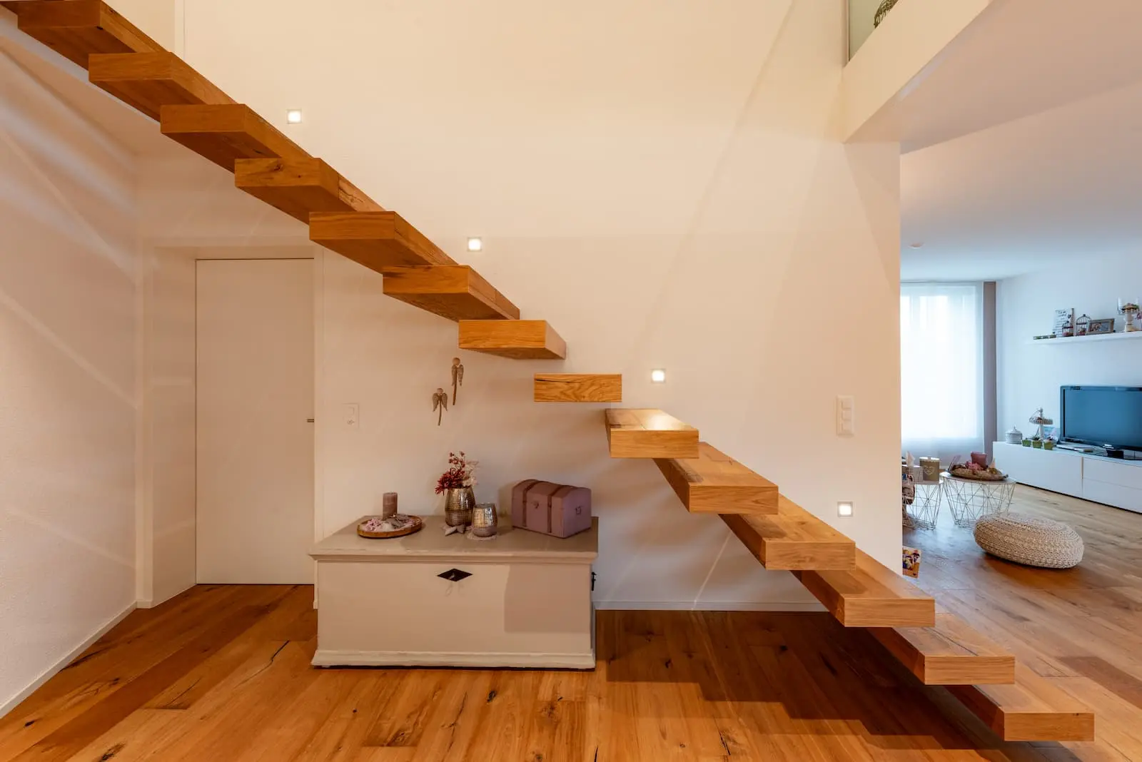 Minimalistische freitragende Treppe aus Massivholz mit integrierter Beleuchtung – zentraler Blickfang im Wohnraum des Einfamilienhauses.