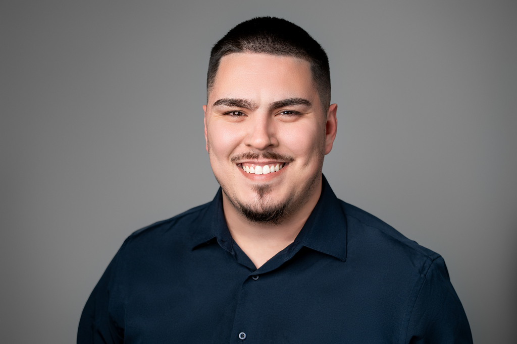 Carlos Sanchez, Account Manager at Coastal Debt Resolve, smiling in a professional headshot wearing a dark navy button-down shirt against a neutral gray background.