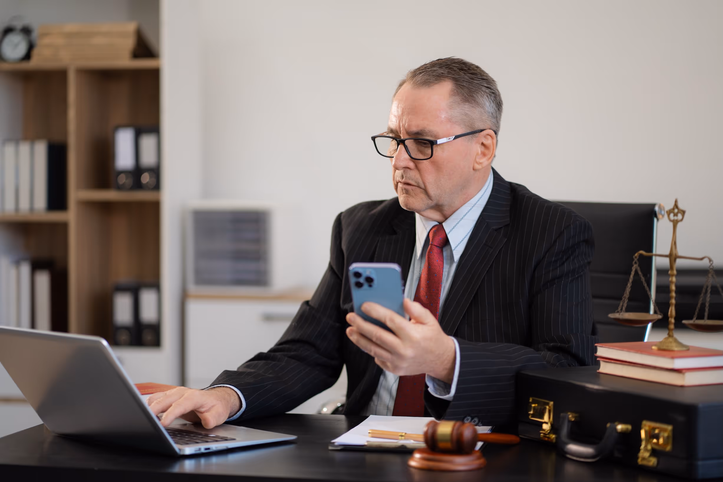 A lawyer  in a dark suit at a desk holding a cell phone reviews possible legal escalation over a missed MCA payment.