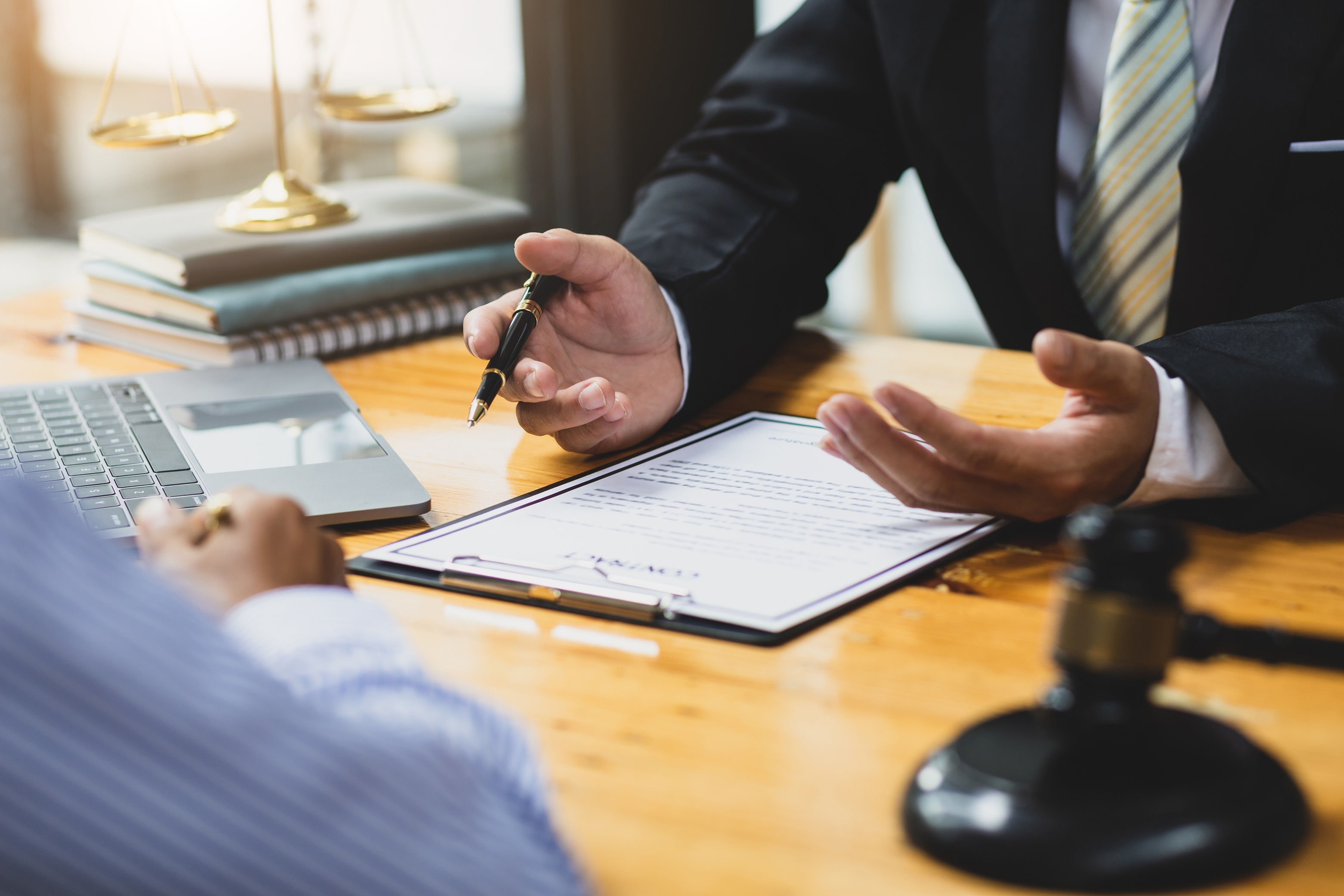 A close-up of a business owner and a financial consultant reviewing a complex commercial financing agreement, with a legal gavel and scales of justice in the background, representing the legal landscape of MCA regulation and how Coastal Debt Resolve helps with MCA debt.