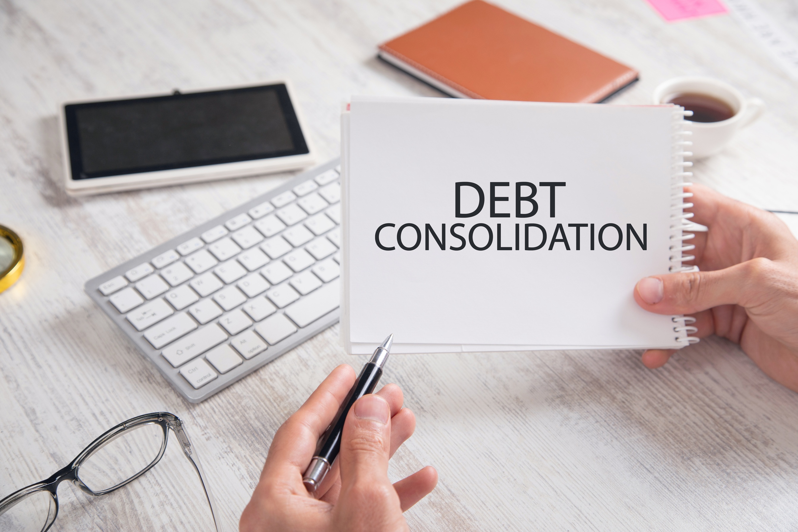 Hands holding an open spiral notebook with 'DEBT CONSOLIDATION' written on the page, representing a business owner seeking financial relief where Coastal Debt Resolve represents a solution.