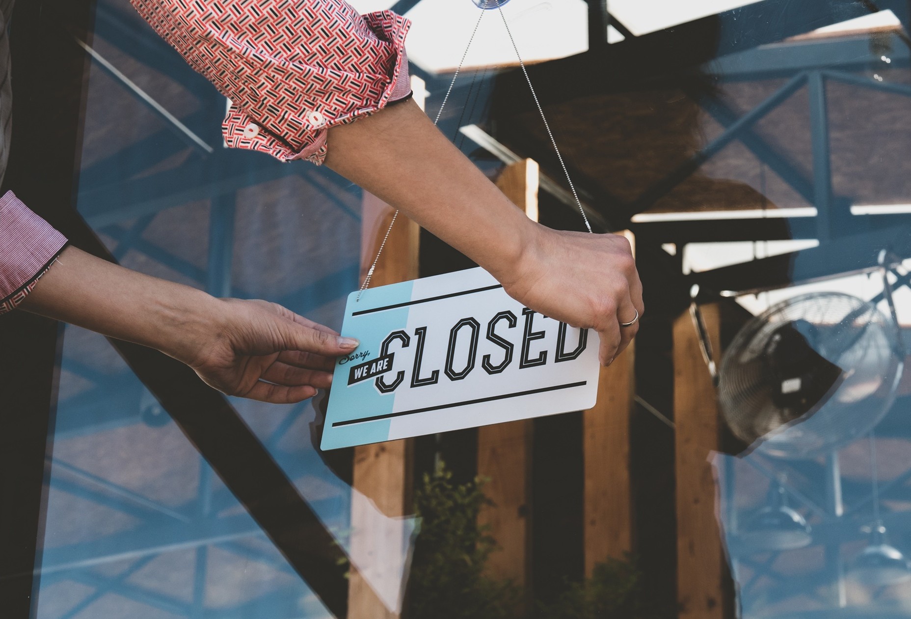 A business owner turning a "Sorry, WE ARE CLOSED" sign on a glass door, representing the financial distress that Coastal Debt Resolve helps prevent with our commercial debt resolution and restructuring services.