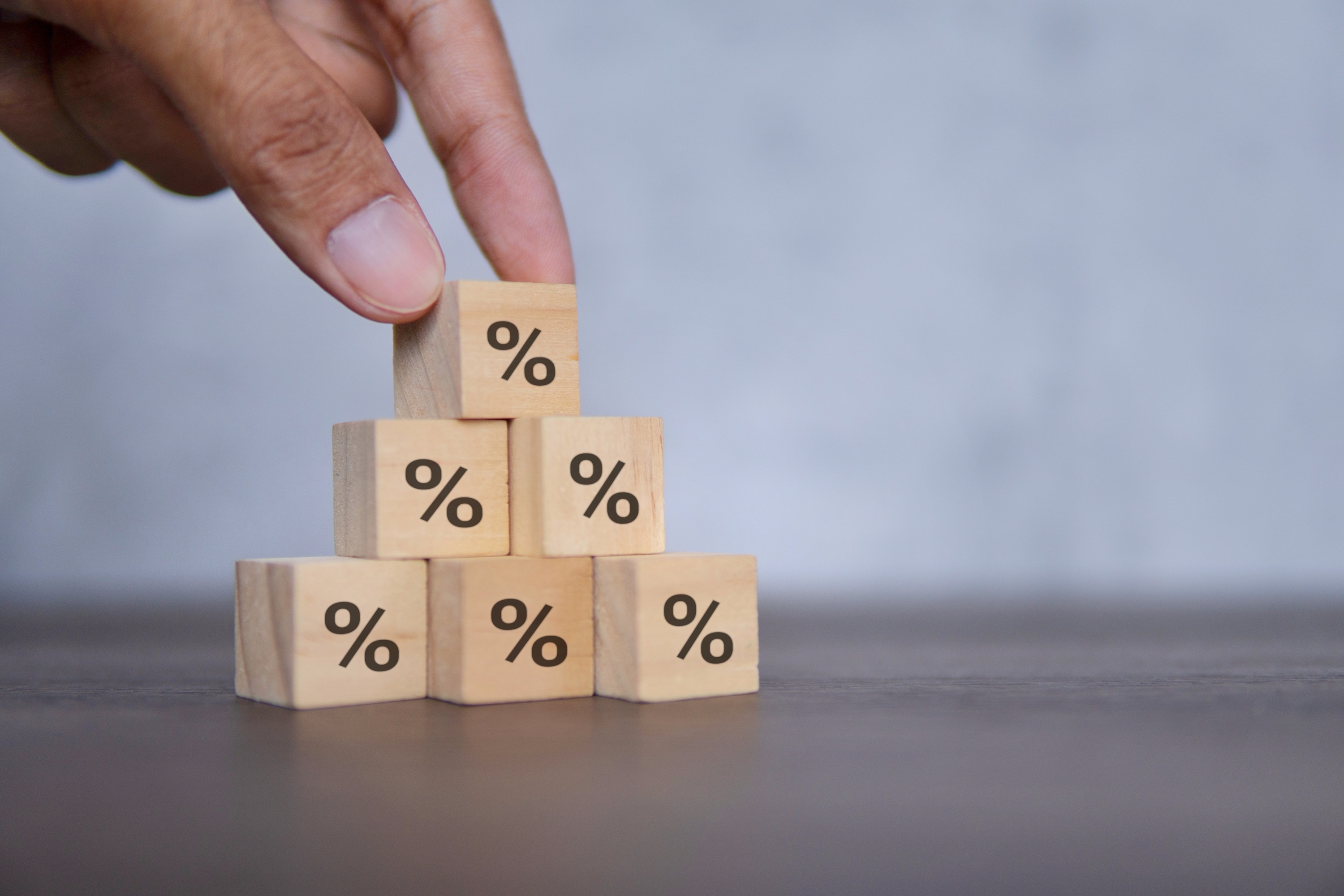 Hand stacking wooden percentage blocks, illustrating business debt restructuring with Coastal Debt Resolve.