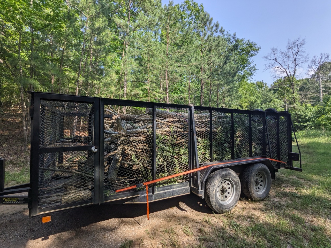 Black trailer loaded with tree branches and logs for hauling away