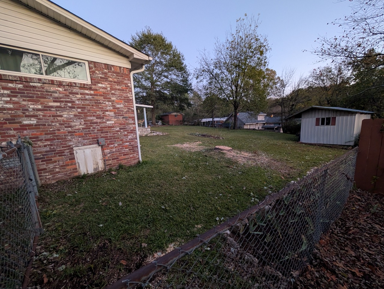 Cleared backyard area with grass and tree removal debris near brick house