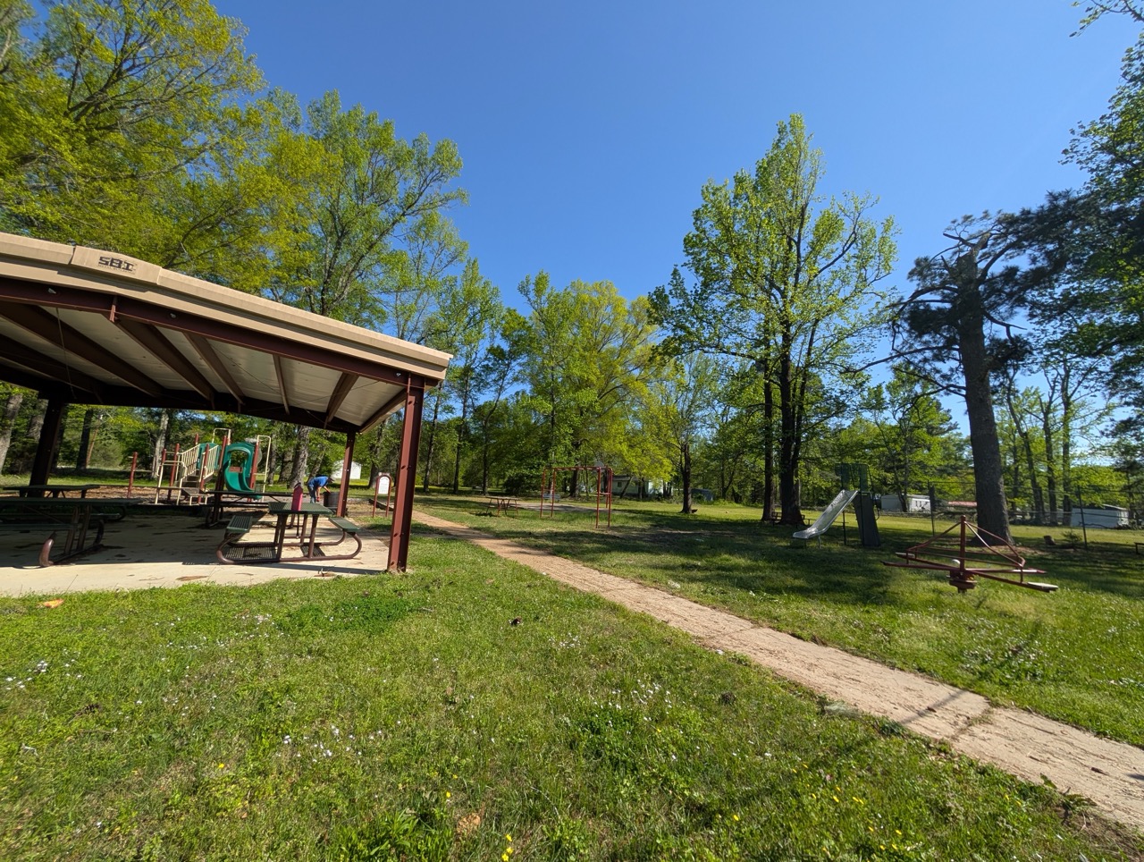 Empty pavilion at public park with green grass and surrounding trees in spring
