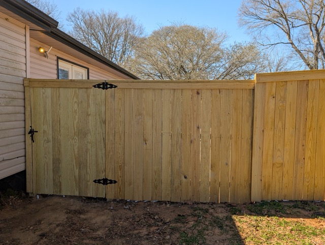 Close-up view of wooden privacy fence gate with black metal hinges