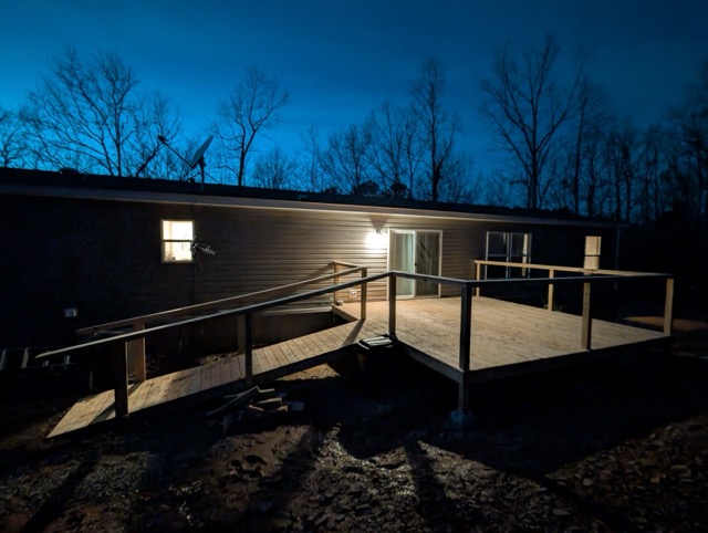 Wide view of completed wooden wheelchair ramp and deck lit by porch light at night