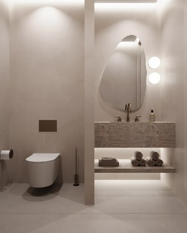 Modern spa bathroom featuring an oval mirror with round wall lights, a minimalist white toilet, and a stone shelf with neatly rolled towels and bath essentials. Soft wall lighting provides a relaxing ambiance.