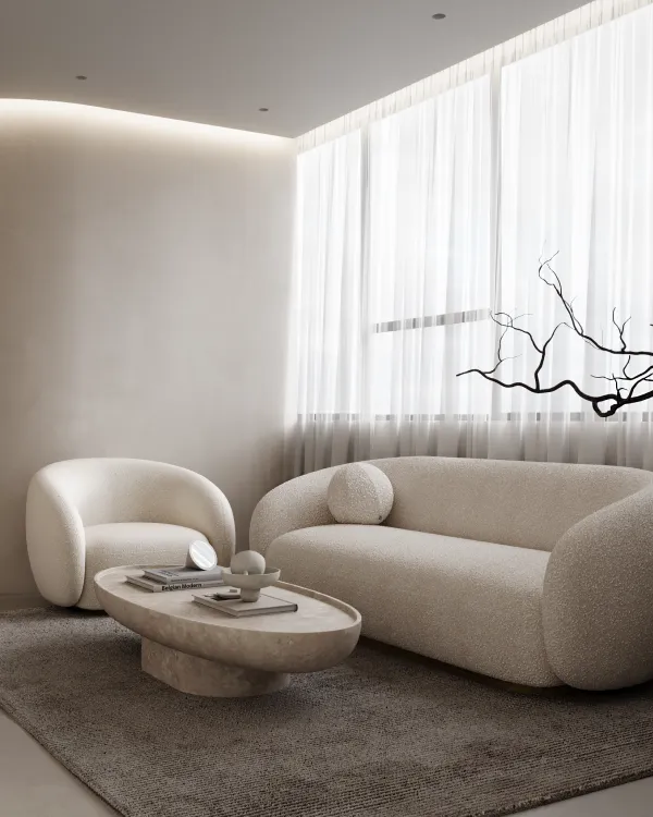 Elegant spa lounge featuring a curved sofa and matching armchair set on a large rug, centered around a stone coffee table with minimalist decor. Soft, diffused light from sheer curtains enhances the tranquil ambiance.
