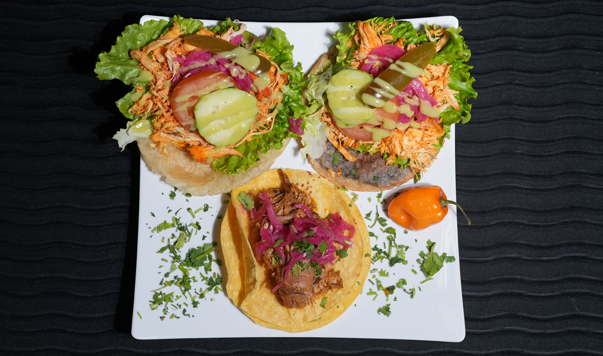 three different tostadas with shredded meat and purple fermented onions, with lettuce drizzled with green sauce