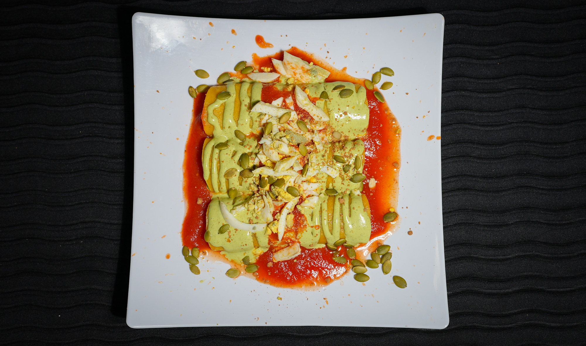 enchilada like dish simmered in green sauce, scattered with pumpkin seeds
