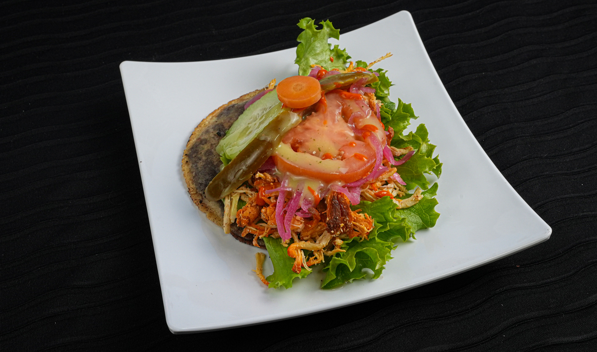 Handmade tortilla filled with pureed black beans, fried and then topped with lettuce, tomato, cucumber, pickle onions, avocado, sauce, and meat