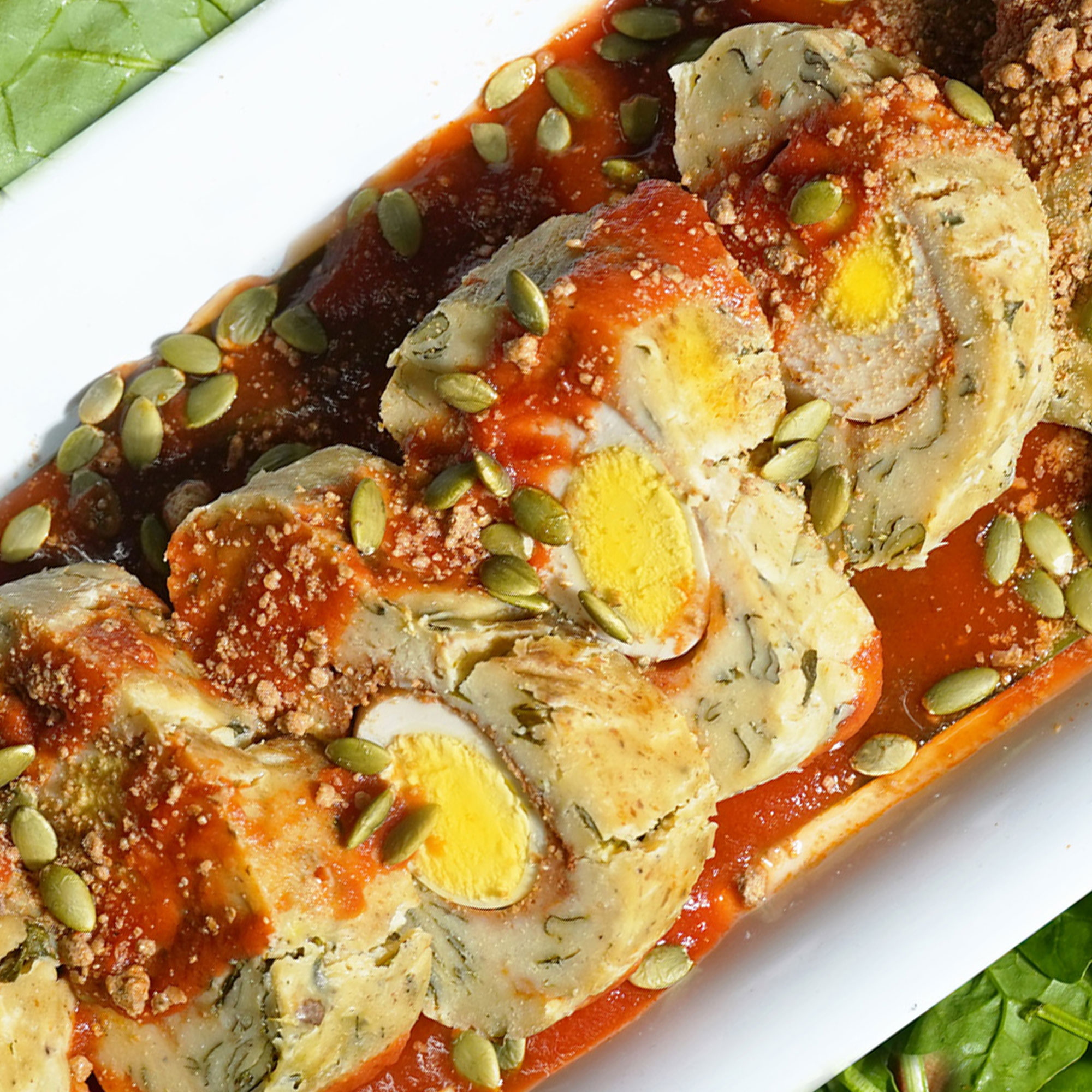 Hard boiled eggs inside tamale dough with loroco flowers. Drizzled in red salsa and scattered green pumpkin seeds