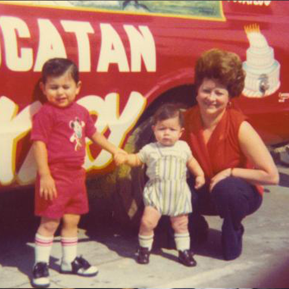 woman with two children in front of a red car