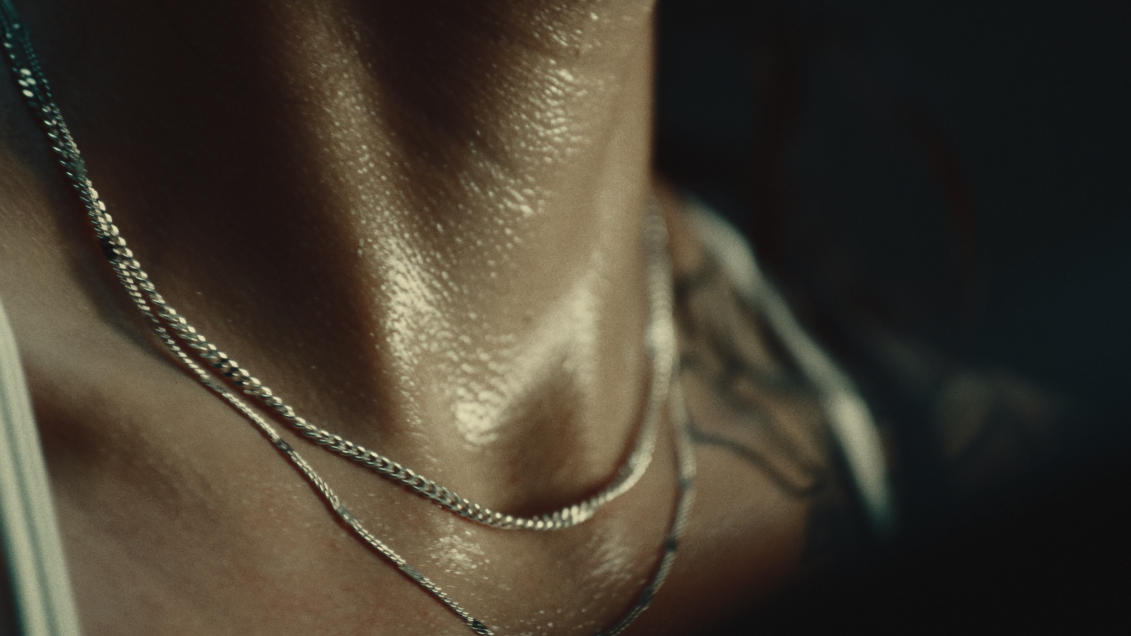Close-up of layered silver chains on an athlete's sweat-beaded neck
