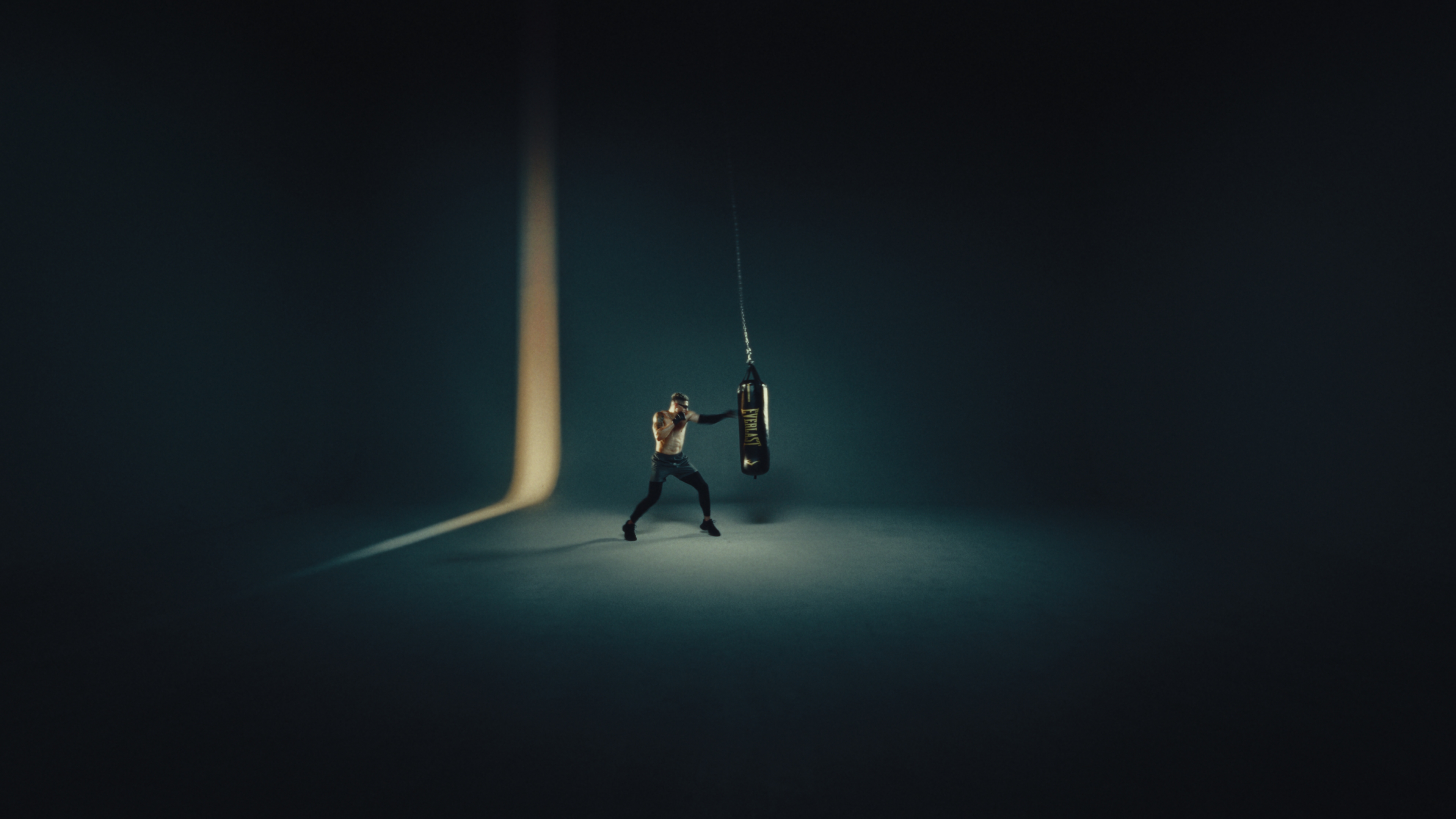 Boxer working an Everlast heavy bag alone on a dark stage under a single shaft of light