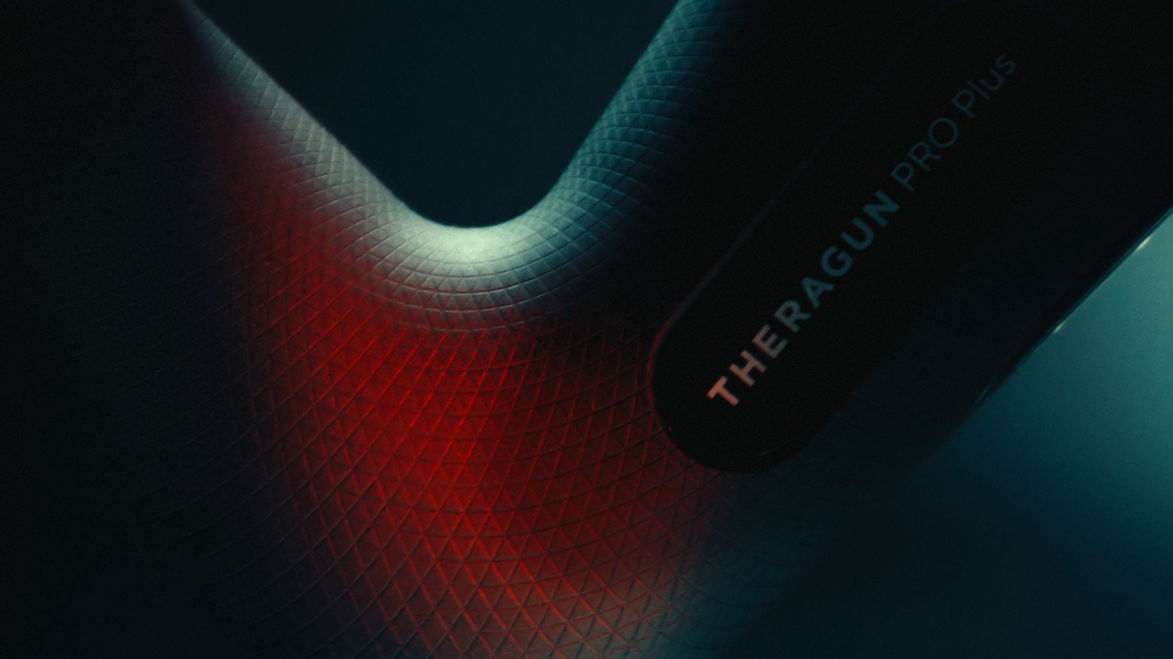 Macro of a Theragun Pro Plus against a textured surface glowing with red light