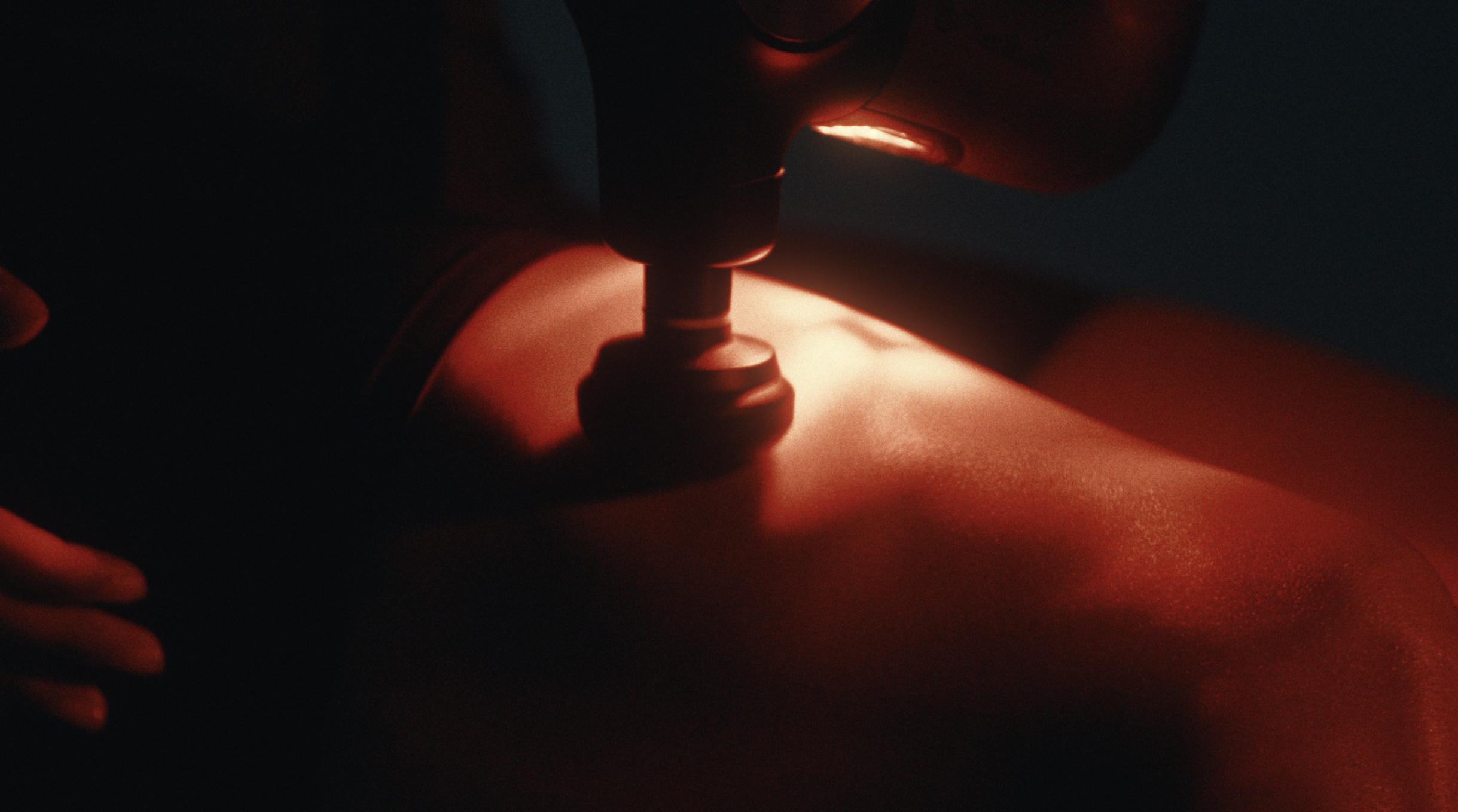 Theragun pressing into an athlete's back in deep red light