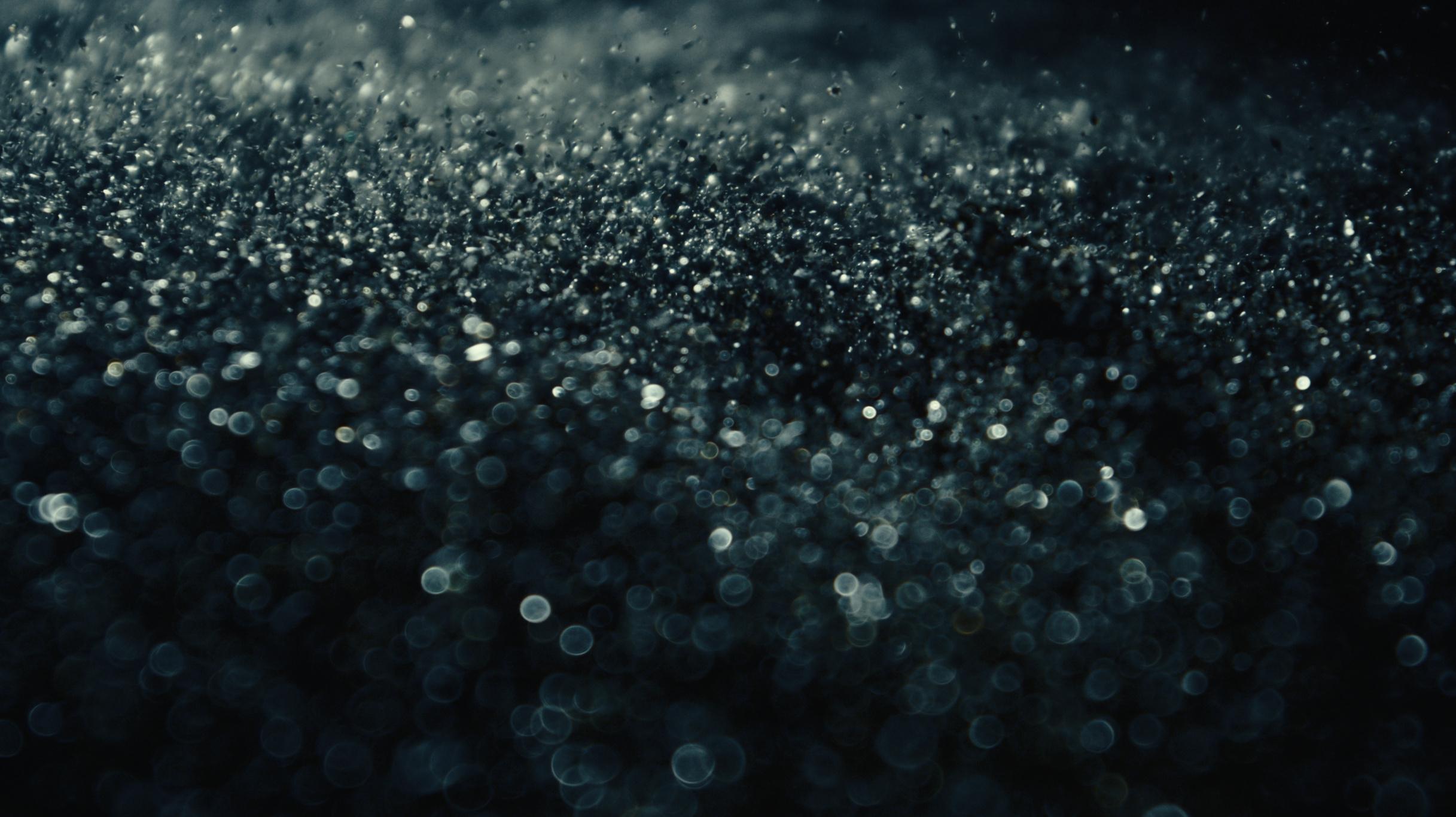 Macro of dark glittering particles drifting in cool light