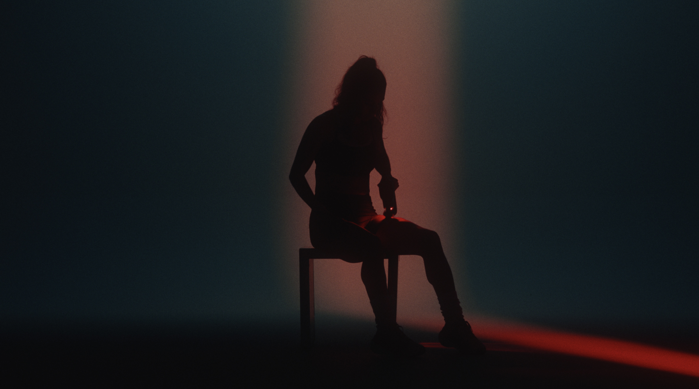 Silhouetted athlete seated in a column of light using a Theragun on her thigh