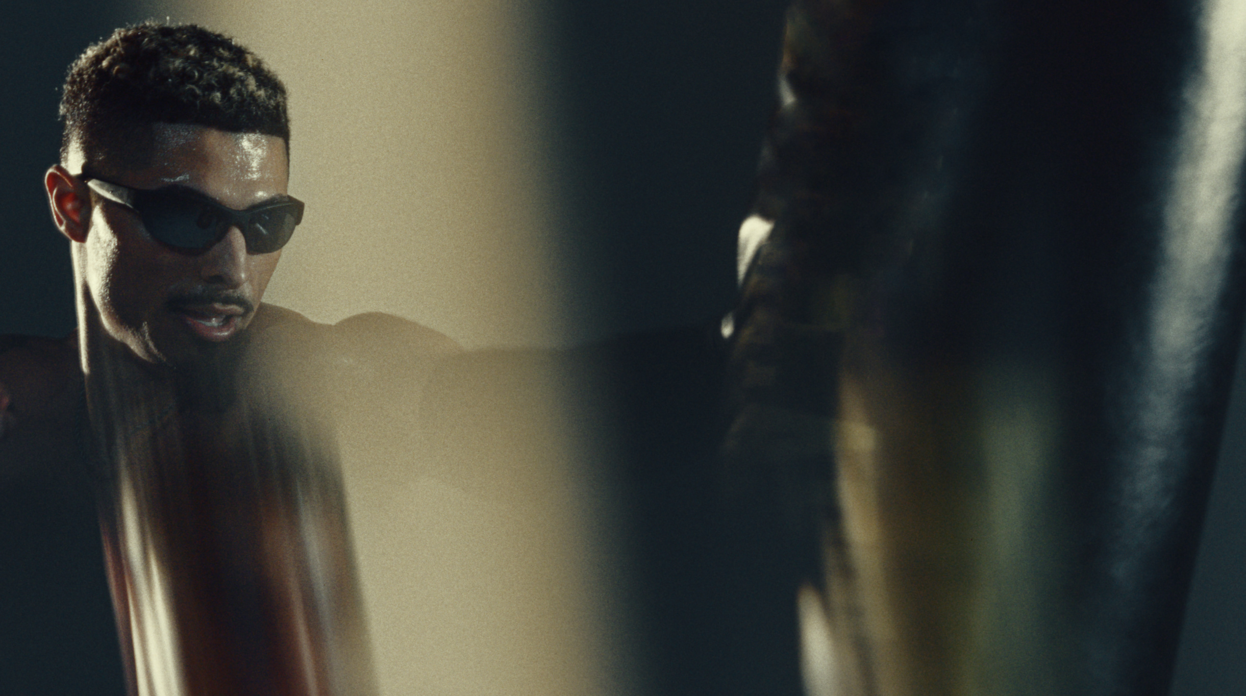 Boxer in dark sunglasses squaring up to a heavy bag