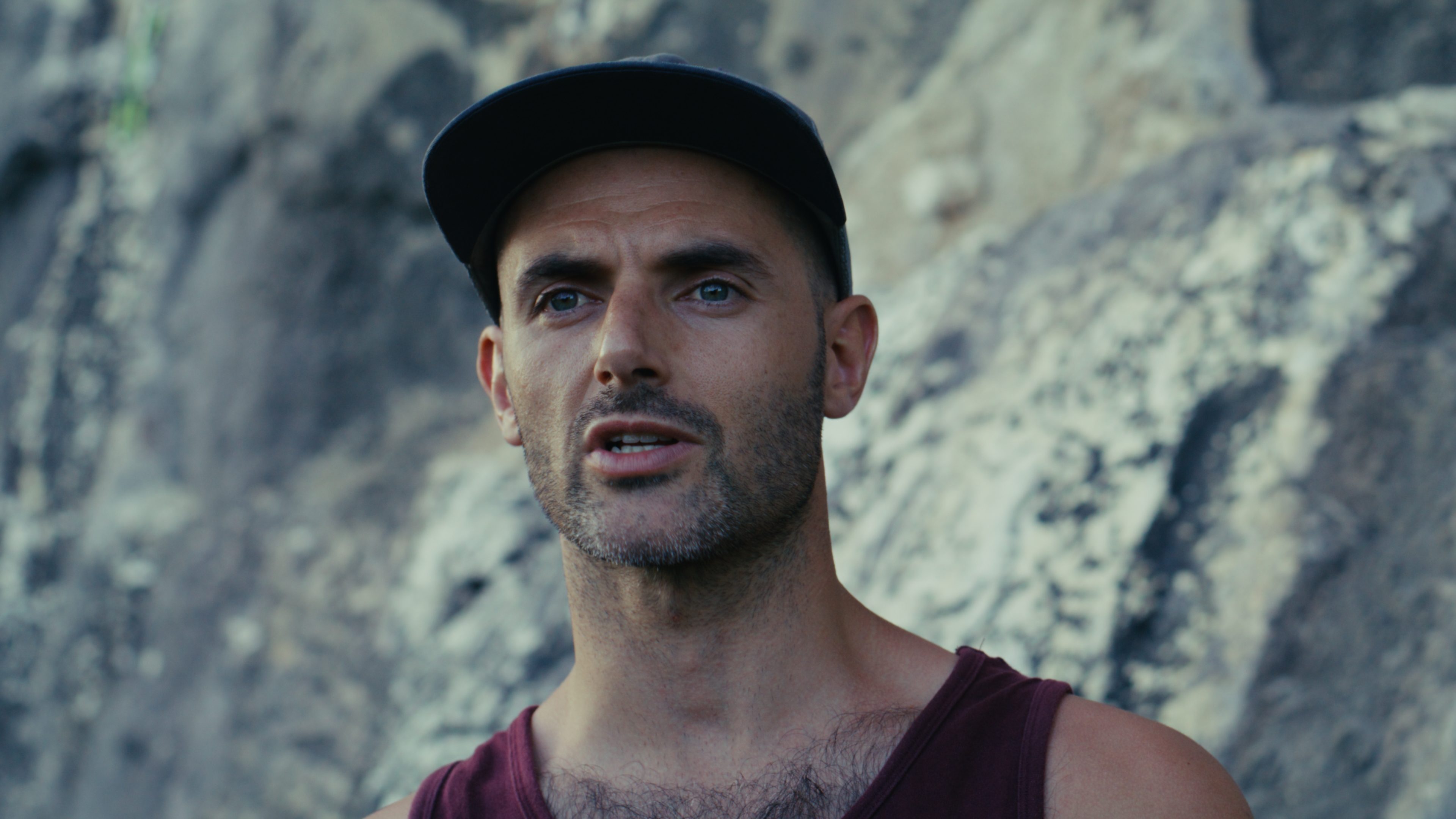 Man in a cap interviewed at the base of a limestone cliff