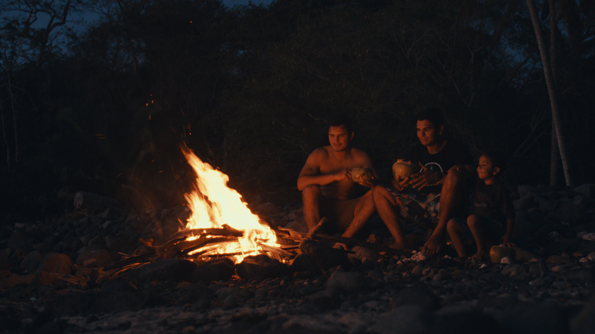 Three friends gathered around a beach campfire at night