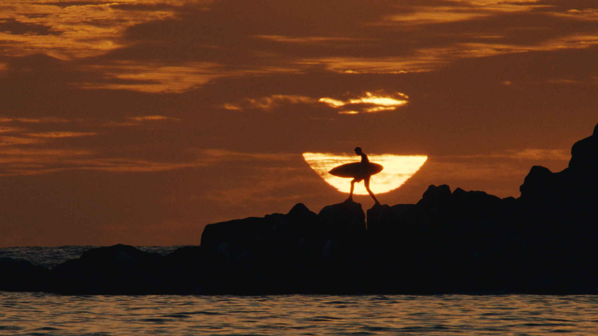 Surfer silhouetted carrying his board against the setting sun