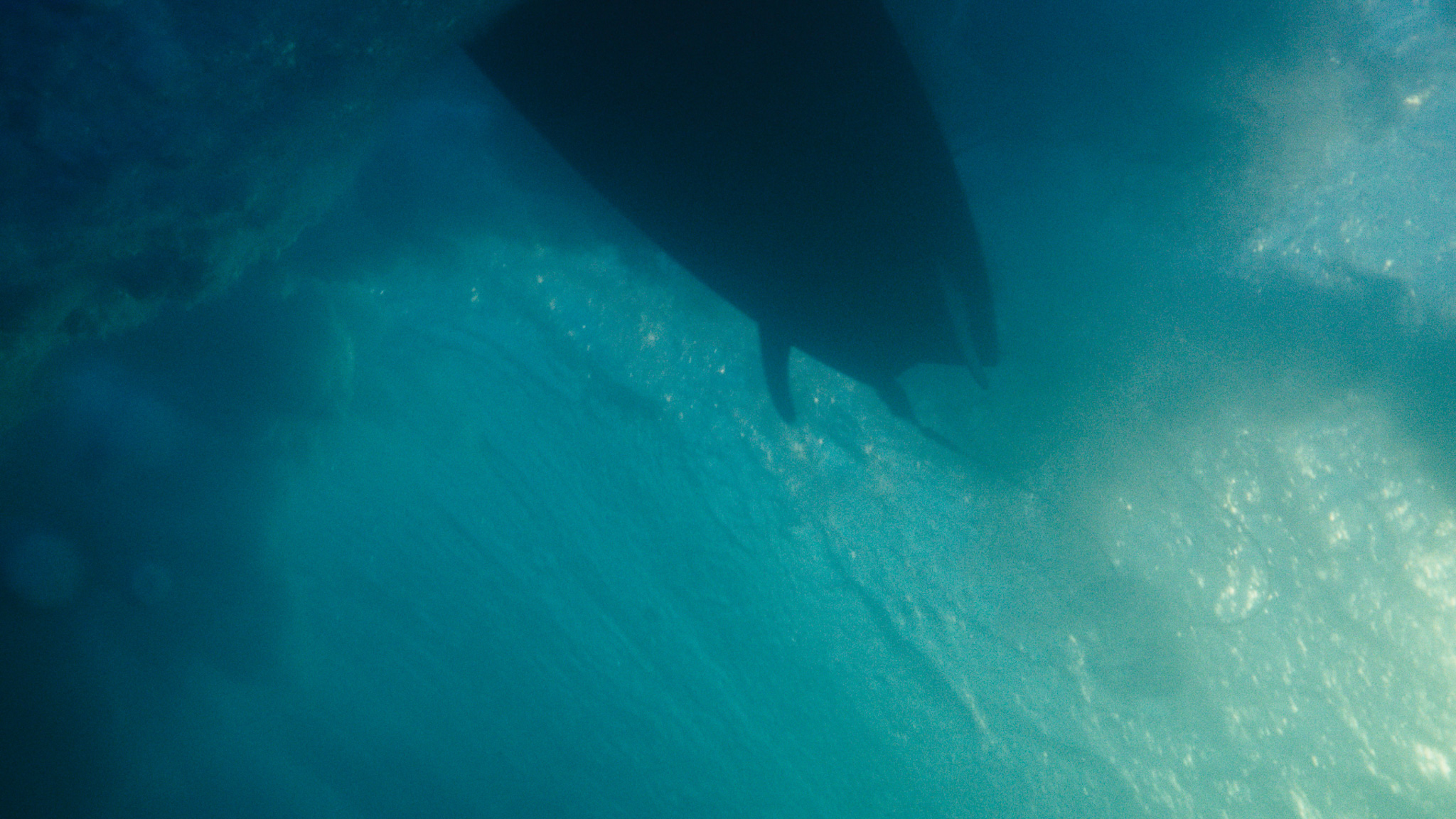 Underwater view of a surfboard hull in turquoise water