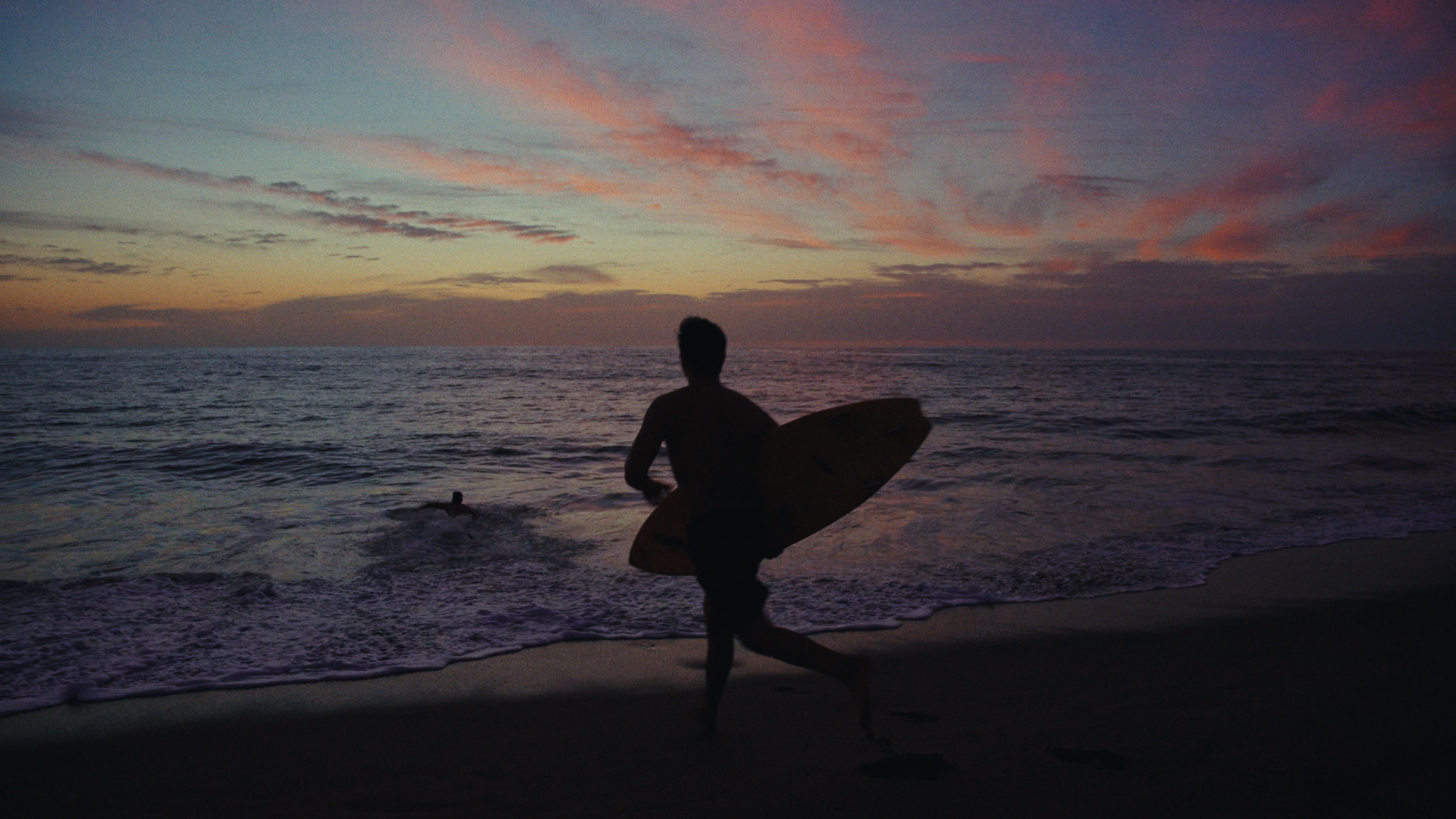 Surfer running along the beach at pink dusk