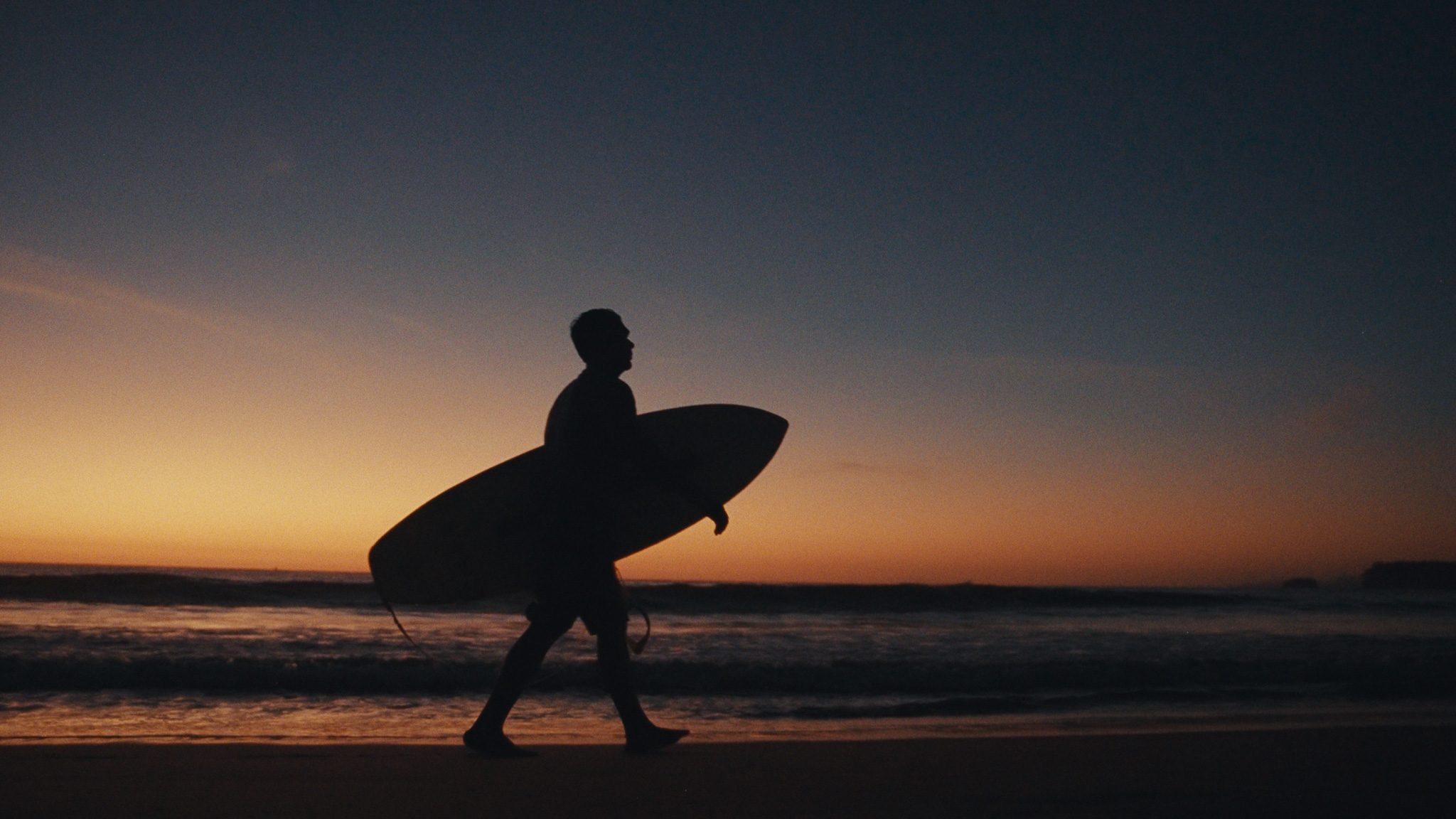 Surfer walking the beach at sunset with his board