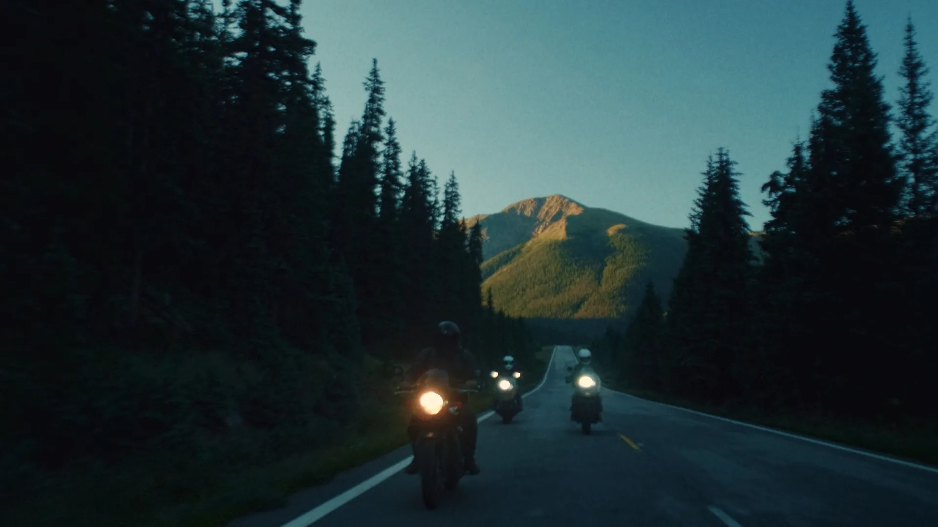 Motorcycle headlights on the road toward a sunset peak
