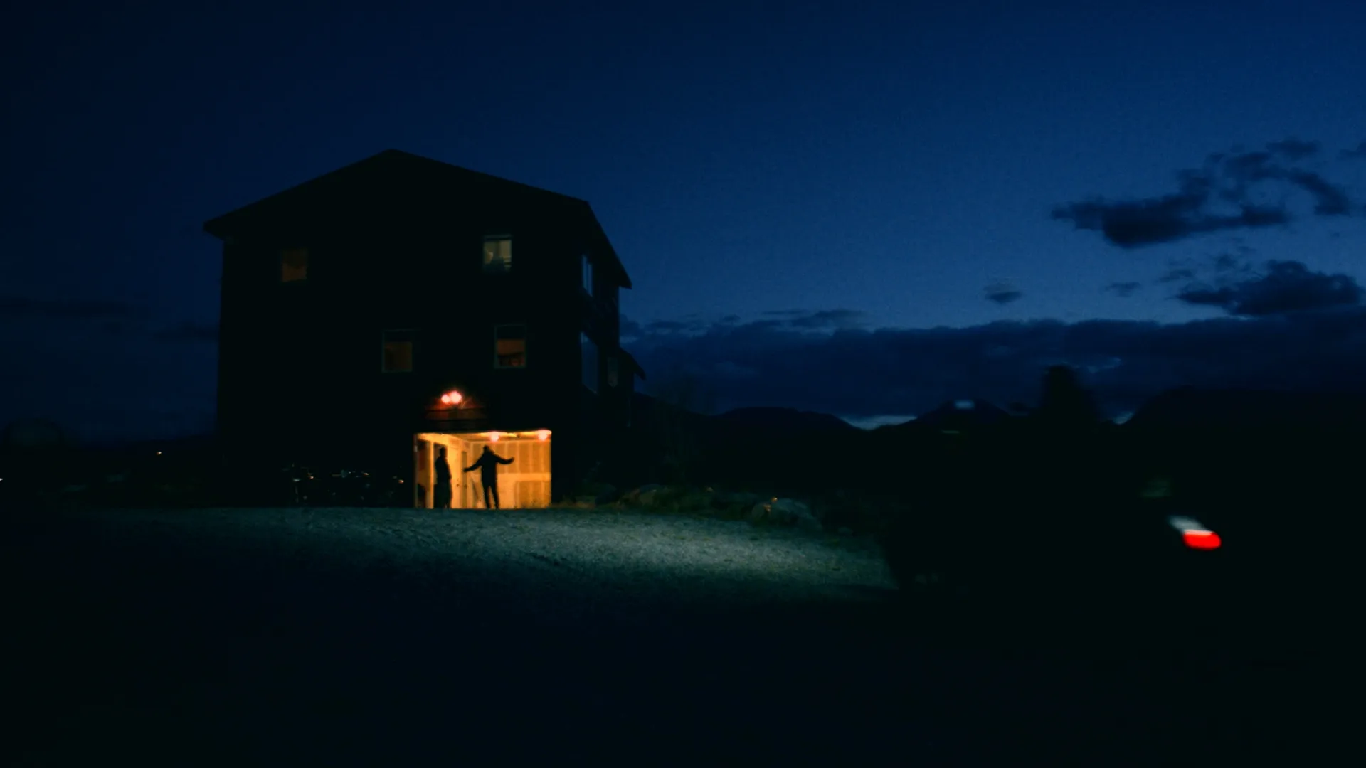 Riders arriving at a lodge at night with a lit doorway